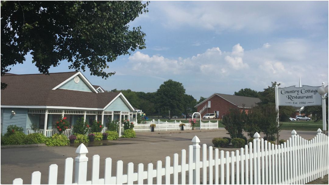 The blue cottage behind its white picket fence, with the Country Cottage Restaurant sign, Est. 1986