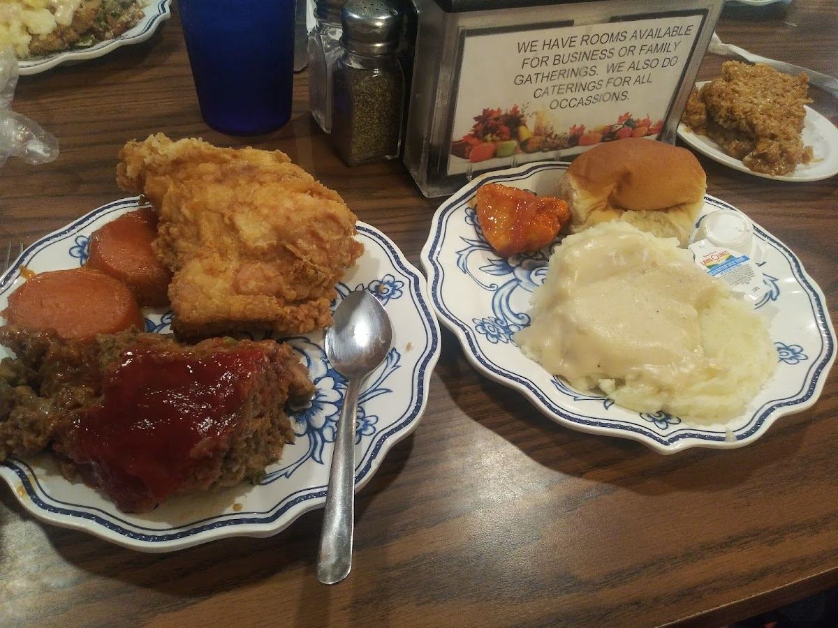 A plate of fried chicken, meatloaf, yams, mashed potatoes and a roll on blue-and-white china